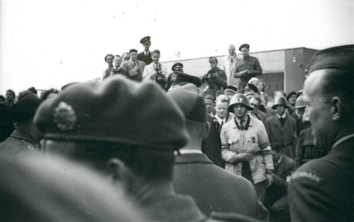 People gathering in front of Hangar B to see Montgomery. Flt Lt Vagn Christensen walks into the frame from the far right wearing his “DENMARK” shoulder flash</i> <i>(Museum of Danish Resistance).